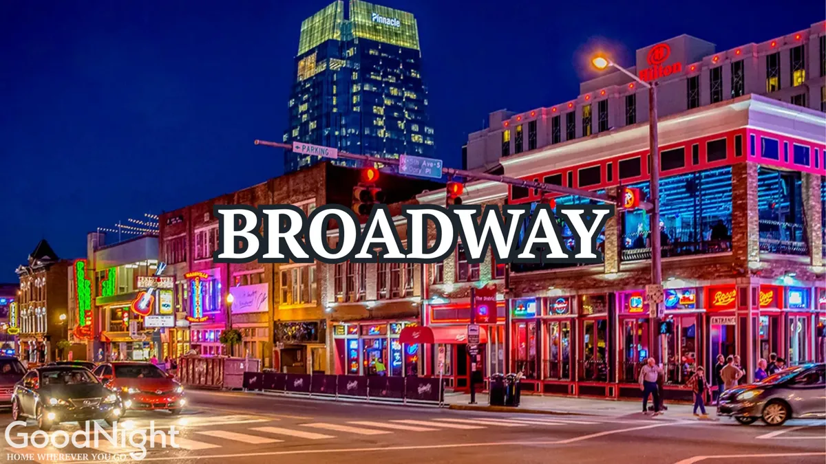 A bustling Broadway street scene filled with illuminated storefronts, people walking, and vibrant nightlife. The Broadway street sign is visible, connecting the image to Nashville's energetic music and entertainment district.