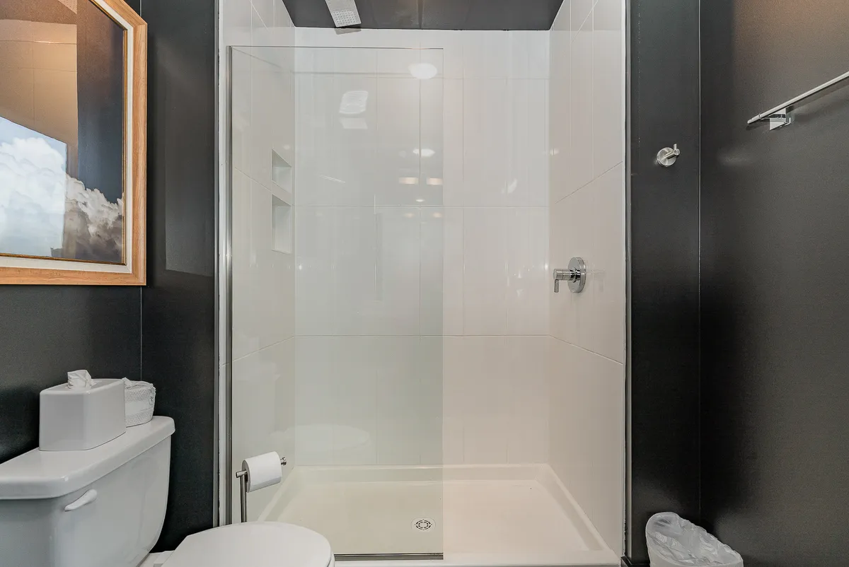 A contemporary spa-inspired bathroom featuring a sleek glass shower enclosure, tasteful framed artwork, a pristine white sink with premium toiletries, and a tranquil ambiance. The space is designed for relaxation and rejuvenation.