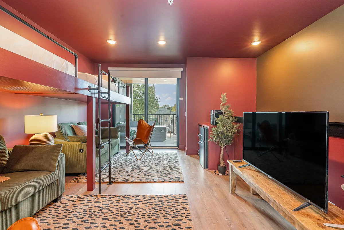 A cozy interior featuring a bunk bed, sofa, television, and balcony view. The arrangement suggests a fun, communal space ideal for movie nights, group hangouts, or winding down with a view after a day out. The presence of both beds and a lounging area aligns well with group flexibility.