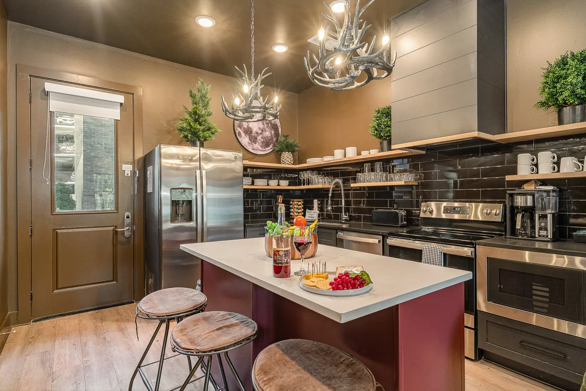 A contemporary kitchen with a prominent island bar, stainless steel appliances, antler-style lighting fixtures, and comfortable bar stools. Decorative plants add a welcoming touch, highlighting the space's suitability for cooking, entertaining, and casual dining.