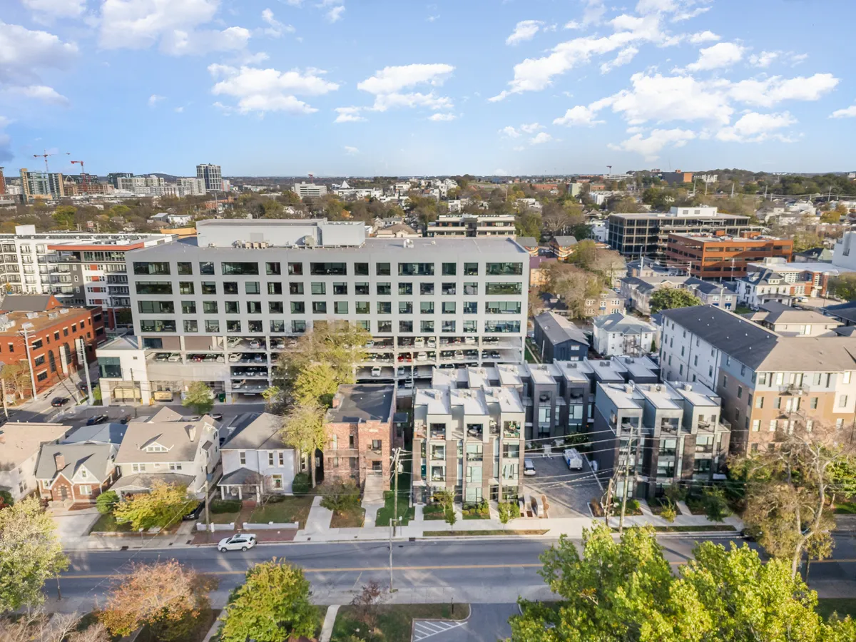 A lively exterior scene featuring a row of modern townhouses and an apartment building set amidst green trees and a bustling street. The image exudes a sense of thriving urban living, community connectivity, and access to local amenities, all key aspects of Music Row’s appeal.