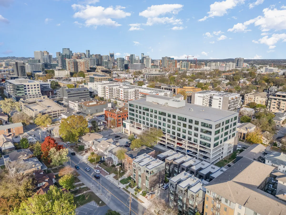 A panoramic view of the downtown Nashville skyline with modern apartment buildings, colorful rooftops, and tree-lined streets at sunset. The image conveys the dynamic urban atmosphere surrounding Rooftop Echo.
