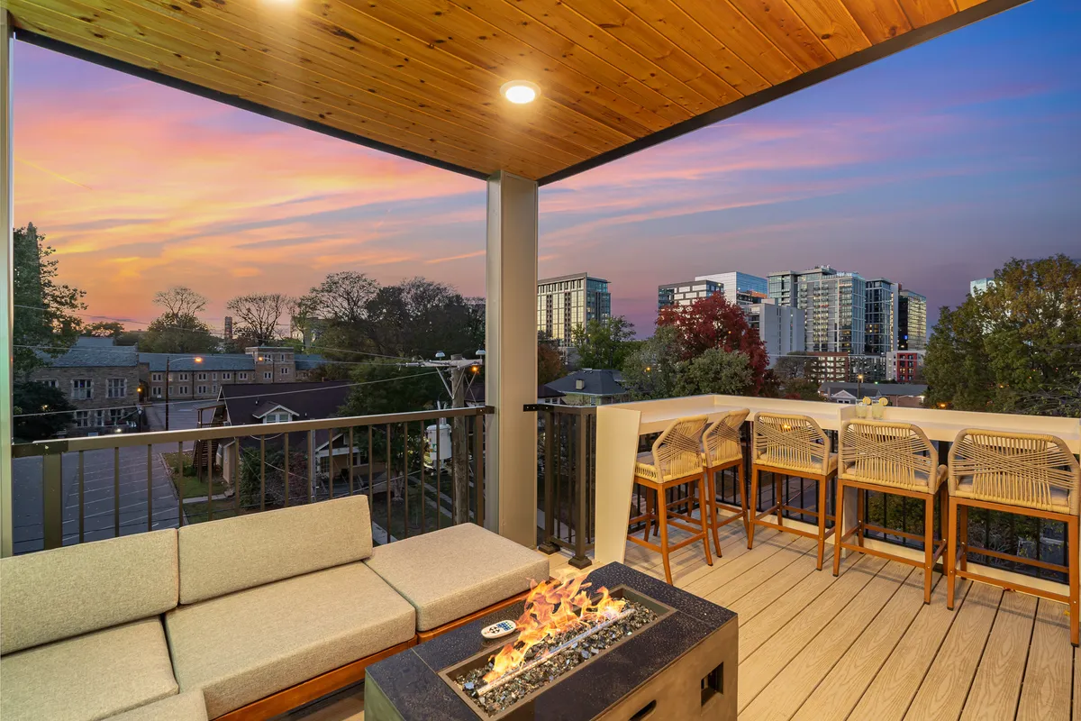 The hero image captures a stylish rooftop deck at sunset with plush sofa seating arranged around a glowing fire pit, bar stools lining a modern counter, and breathtaking views of the Nashville city skyline in the background. The setting radiates warmth and sociability, perfect for evening gatherings and making memories with friends or family.